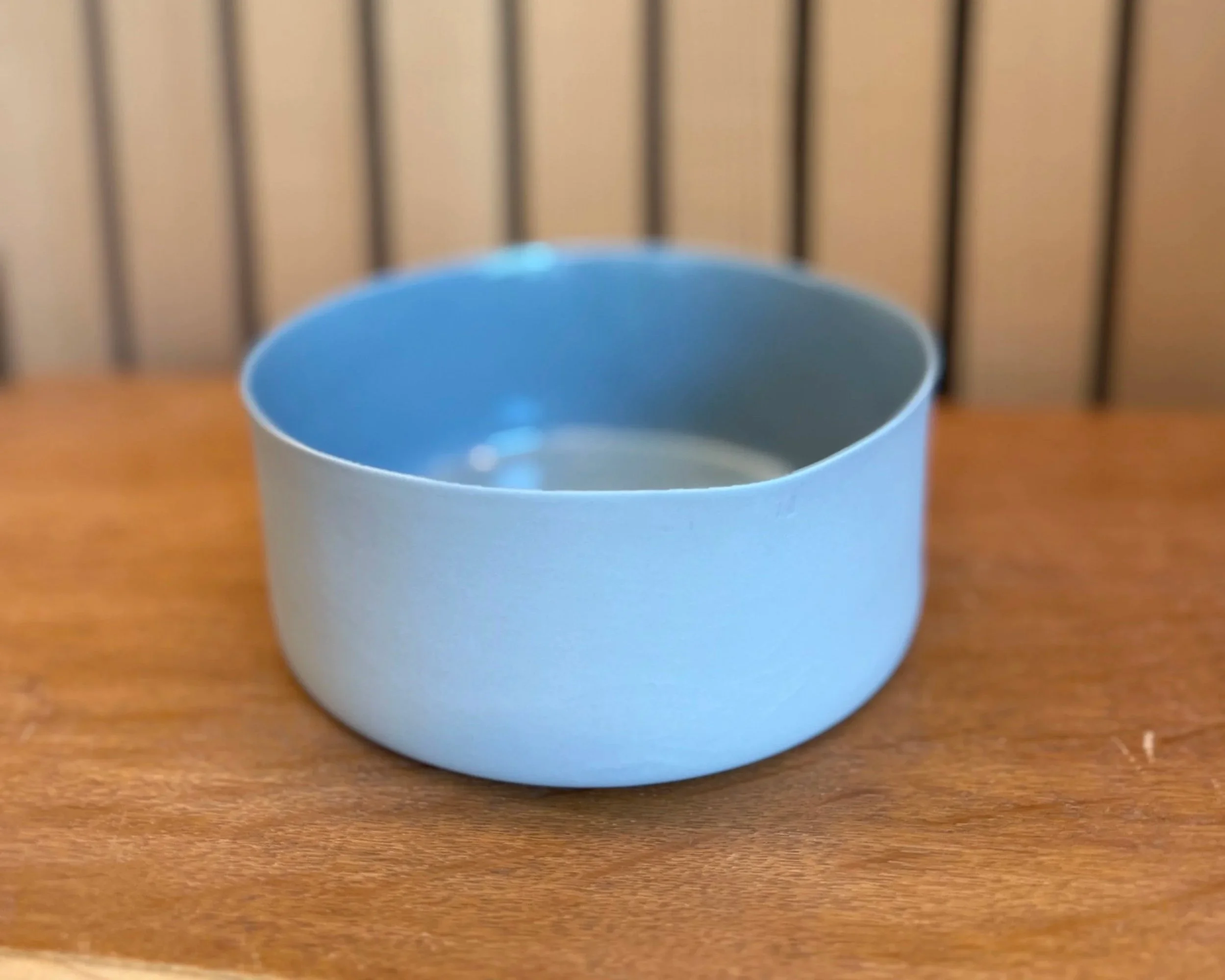 Leerer silberner Tortenring auf einem Holztablett vor einem Holzrücken.