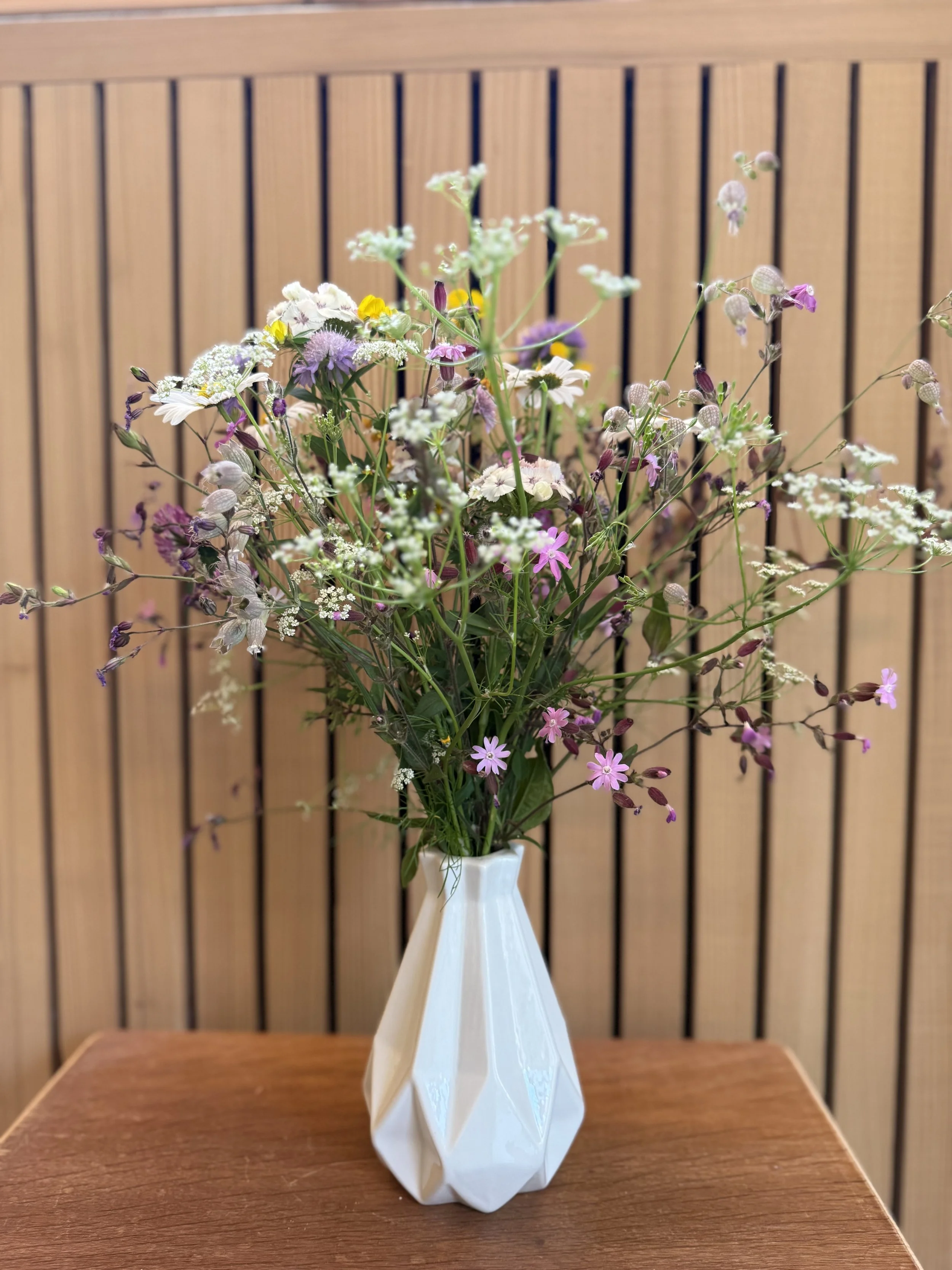Bunter Blumenstrauß in einer weißen Vase auf einem Holztablett, vor einer Holzplatte