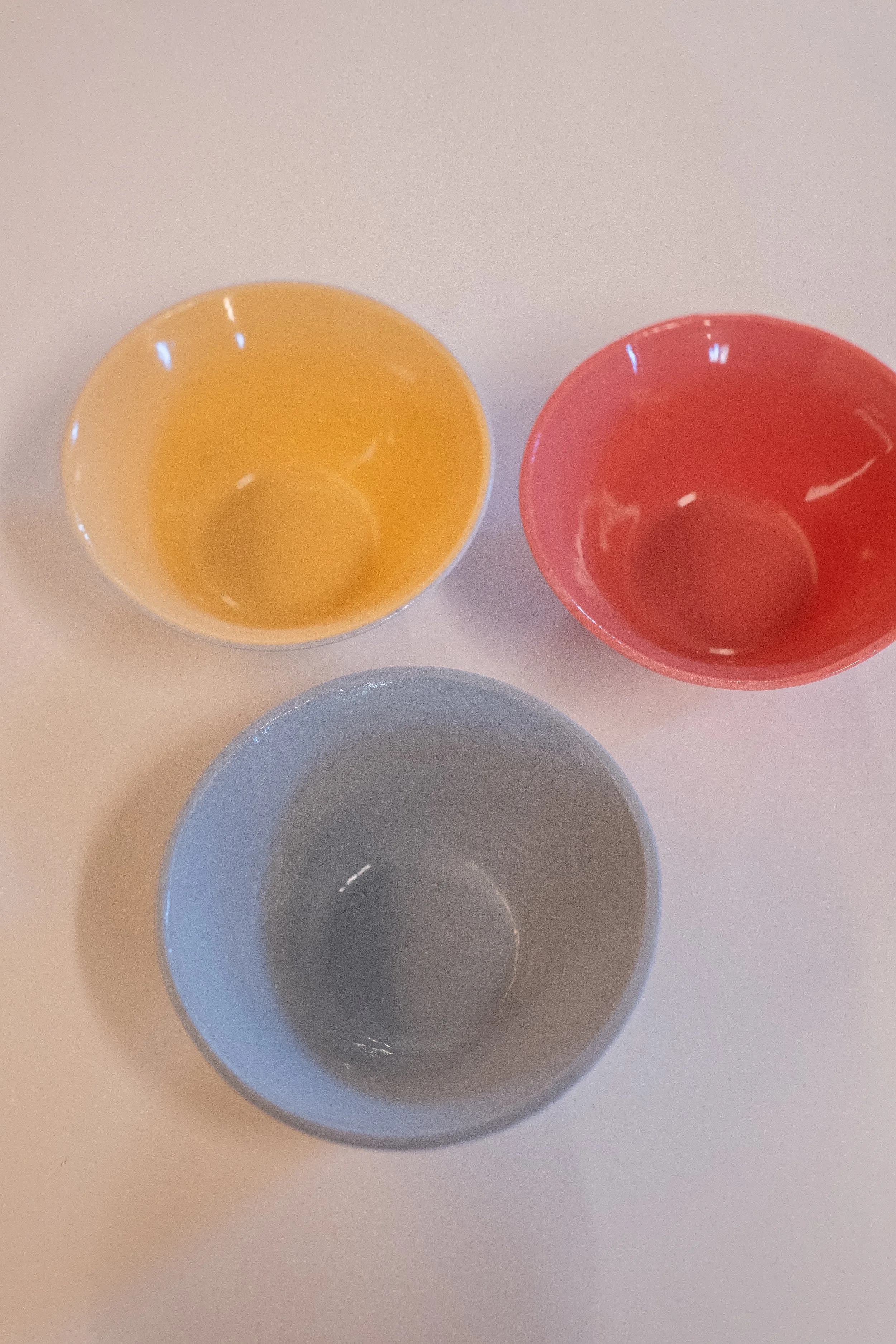 Drei bunte Tassen in Gelb, Rot und Grau auf einer weißen Oberfläche.