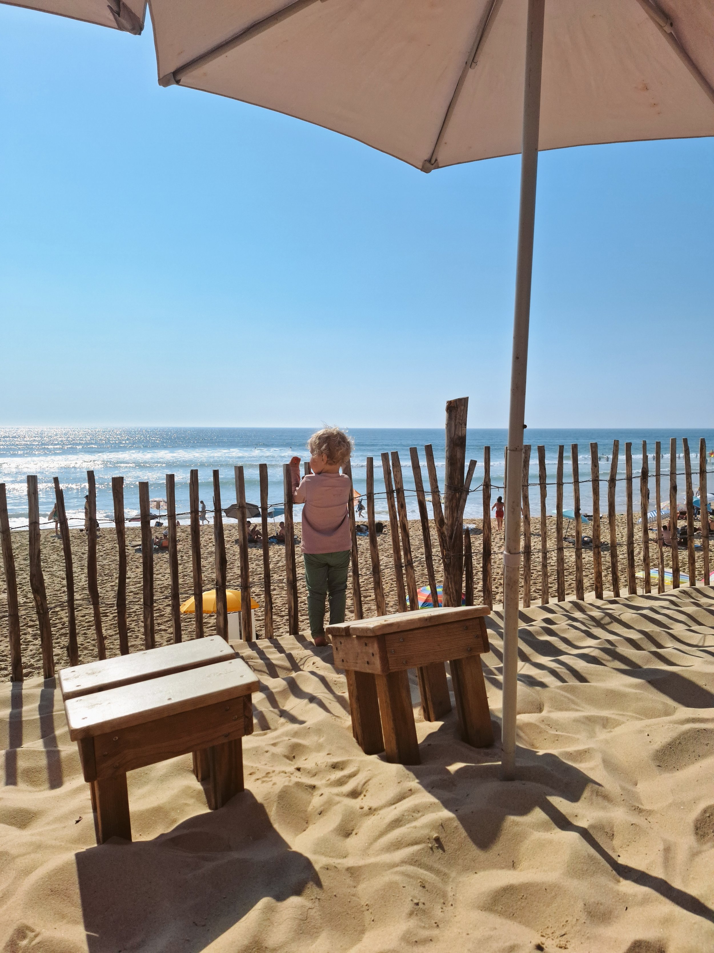 Kind schaut am Strand hinter einem Zaun Richtung Meer