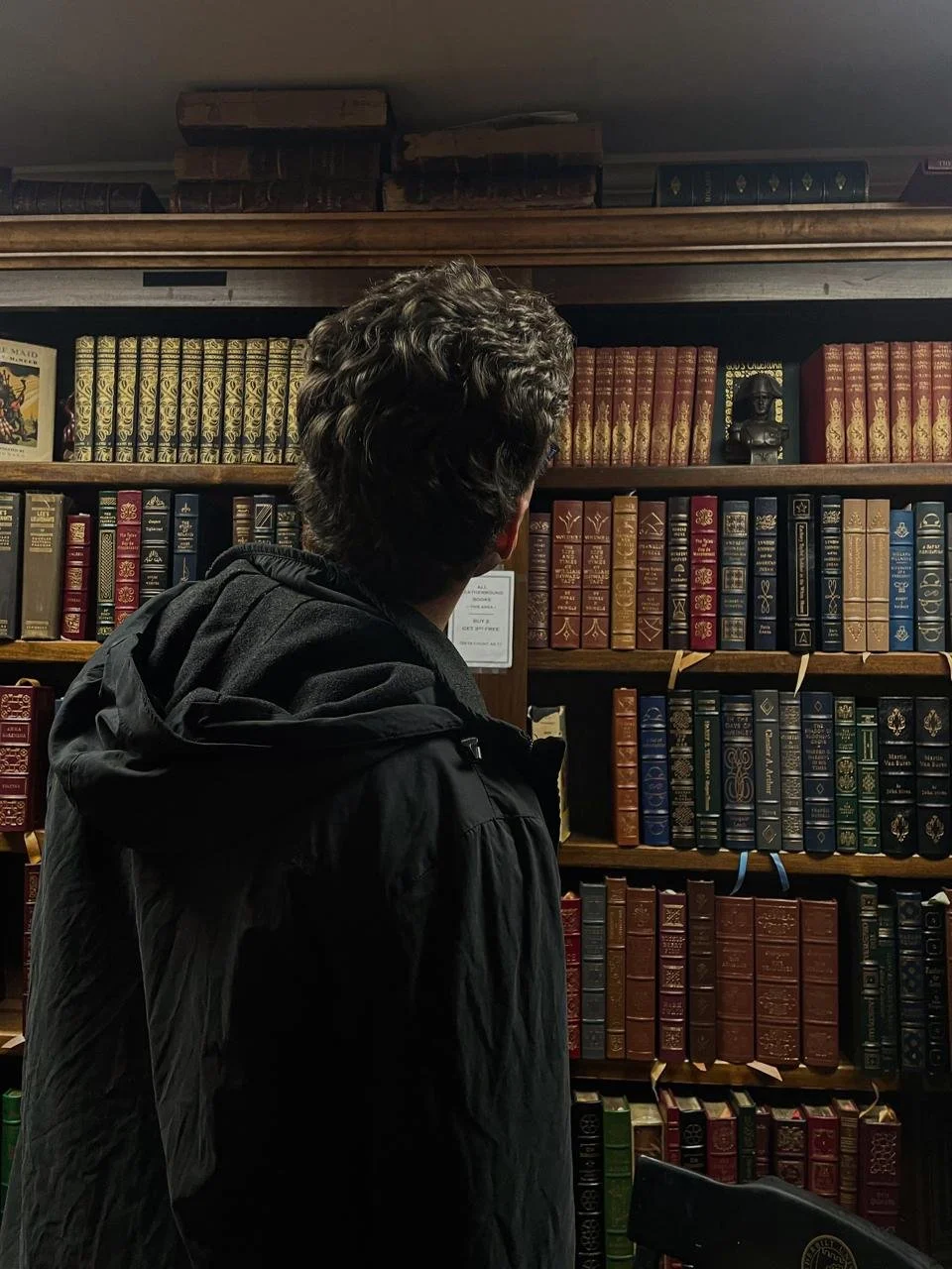 Person in black jacket looking at bookshelf filled with colorful books in a library or bookstore.