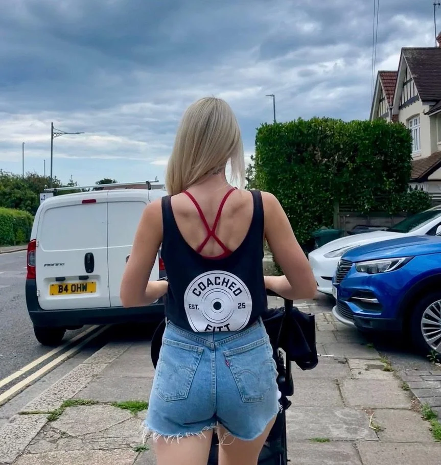 Woman with blonde hair seen from behind standing on a sidewalk near parked cars on a cloudy day