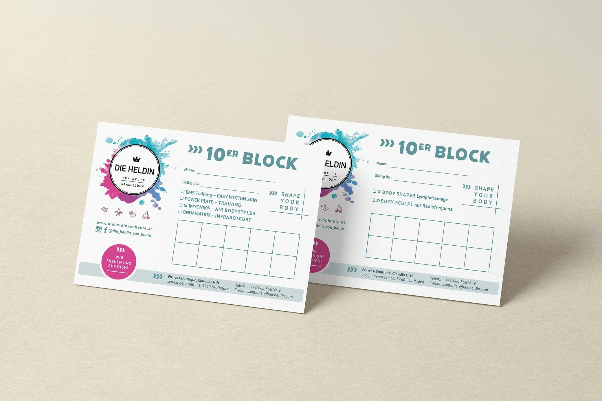 Zwei Flyer für das Fitnessstudio die Heldin. Die Flyer sind vor einem neutralen Hintergrund platziert, mit bunten Wasserfarbenspuren im Hintergrund. Sie enthalten Informationen zu Kursen, Kontakt, und Social Media, mit einer pinken Sprechblase, die auf ein Angebot hinweist.