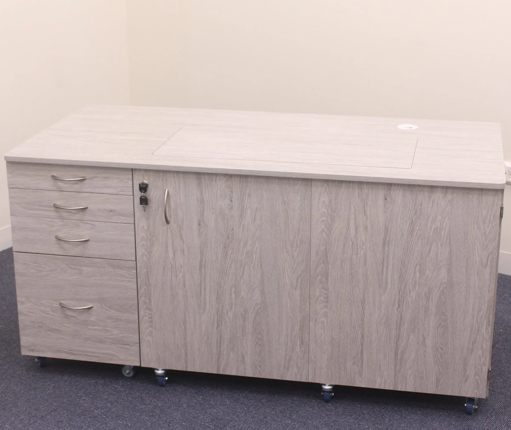 A light wood-colored cabinetry with four drawers on the left and two doors on the right, set on caster wheels against a beige wall.