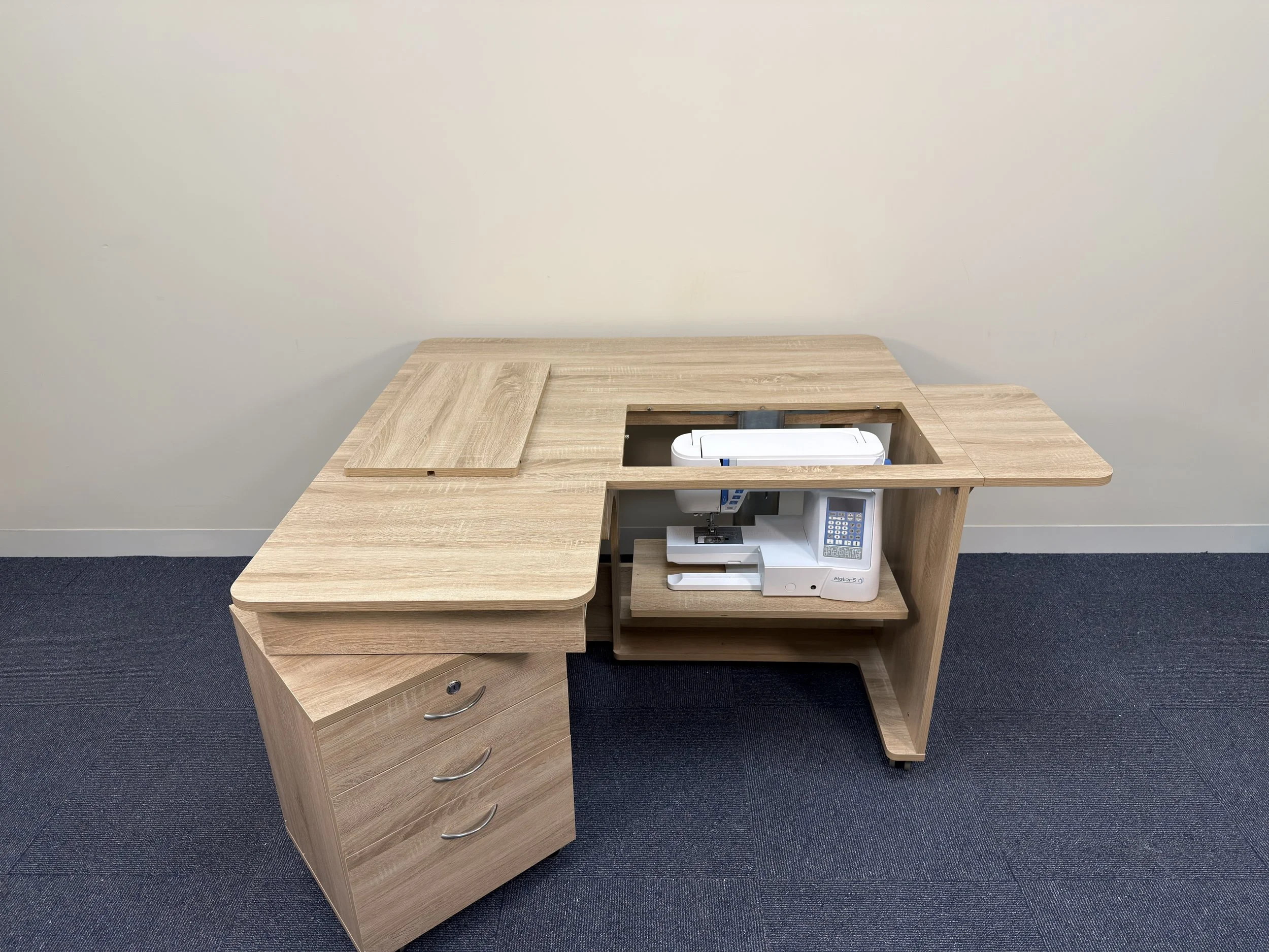 Wooden office desk with a built-in safe, a flat surface, and drawers on the left side, set against a plain wall on a blue carpeted floor.