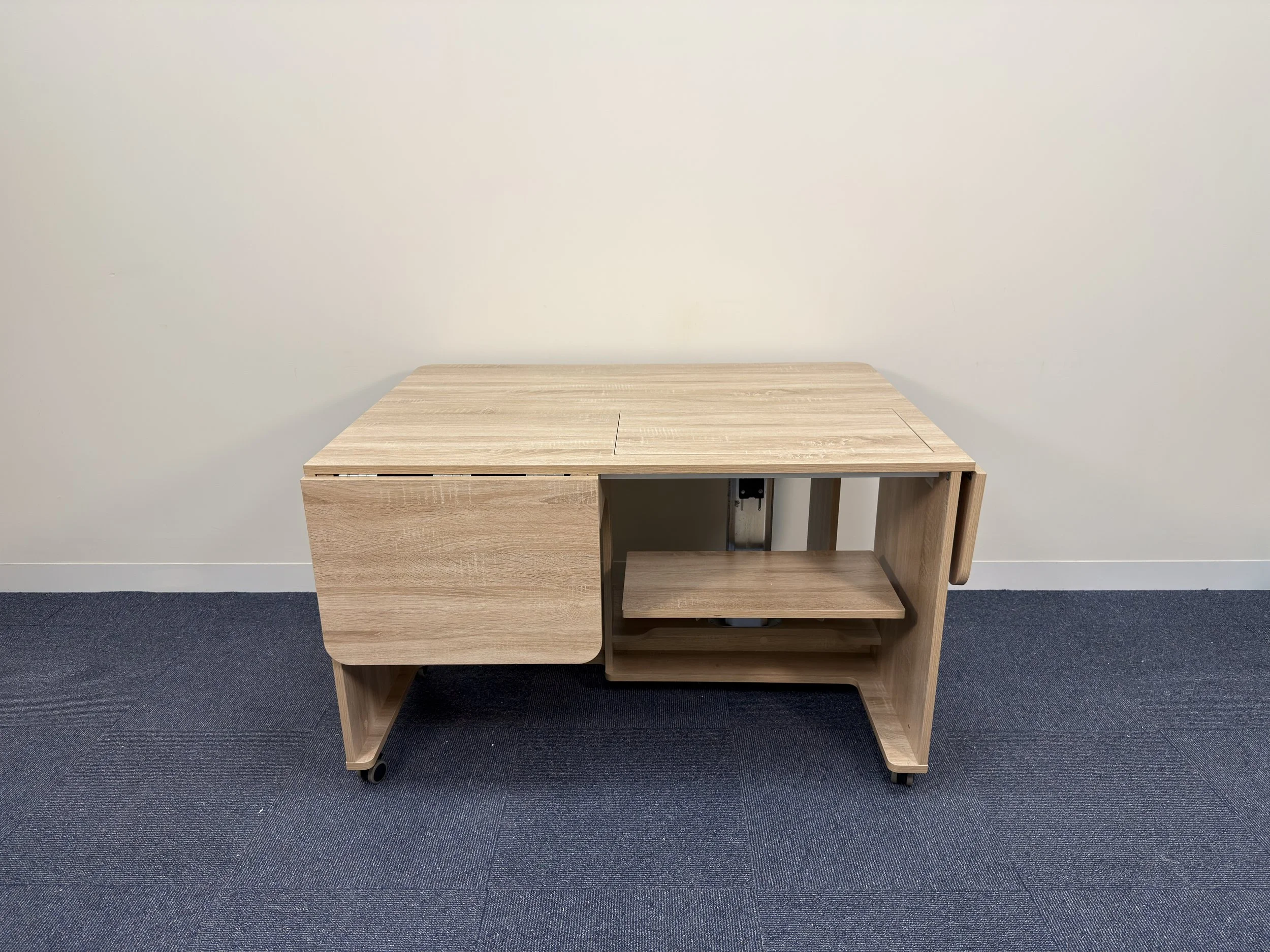 Light wood rolling desk with closed cabinet and open shelf, on a blue carpeted floor, against a plain white wall.