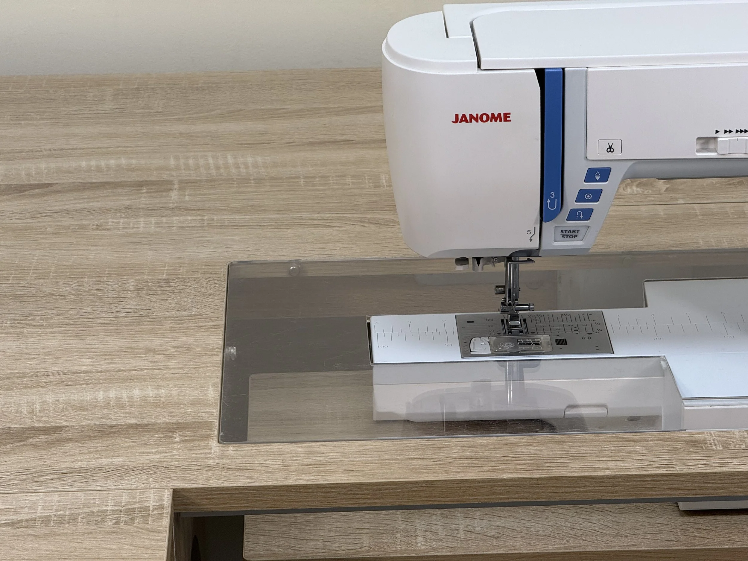 A Janome sewing machine on a wooden table with a transparent extension table.