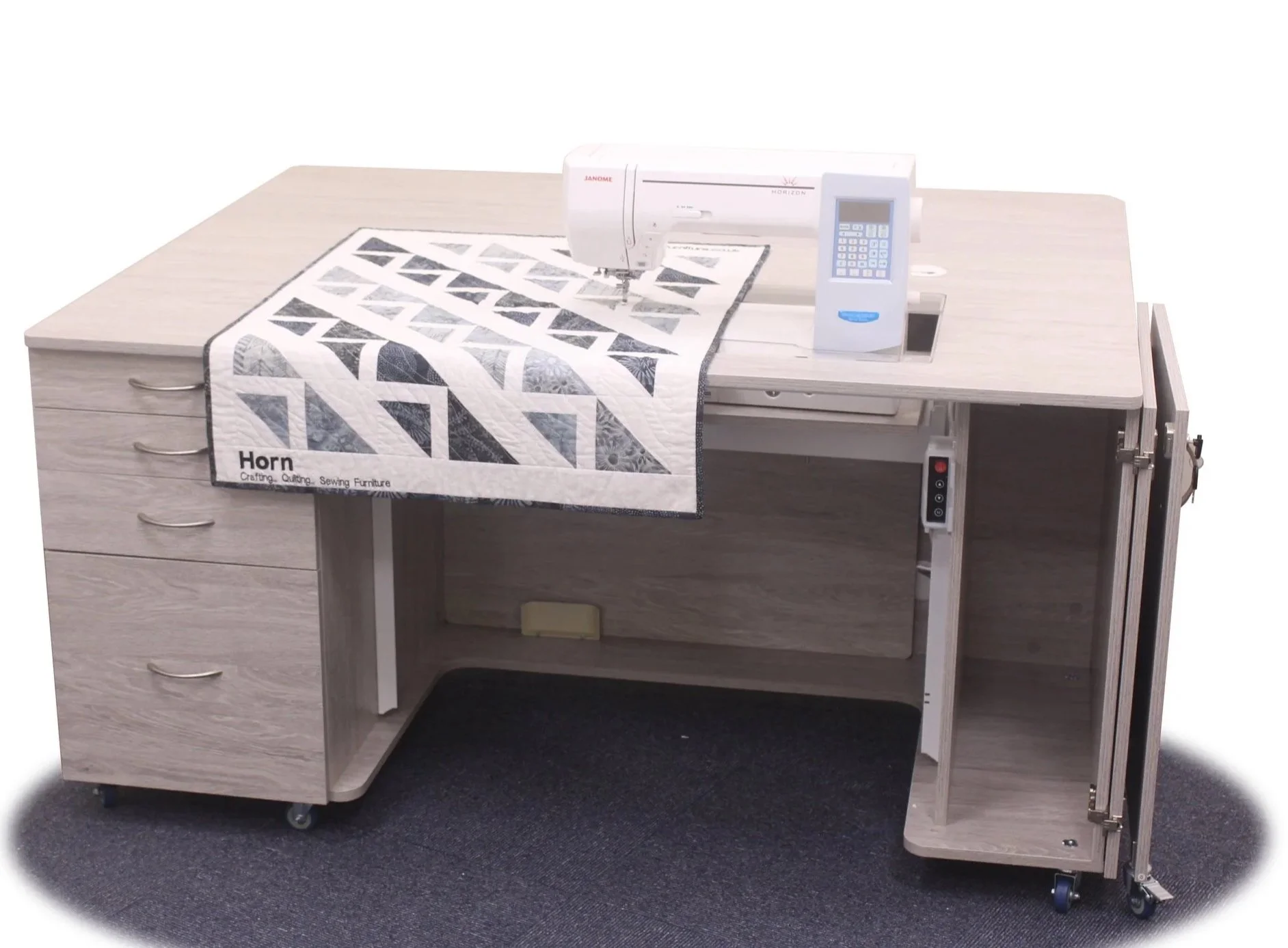 A sewing machine on a desk, with a quilt featuring black and white geometric patterns draped over the side.