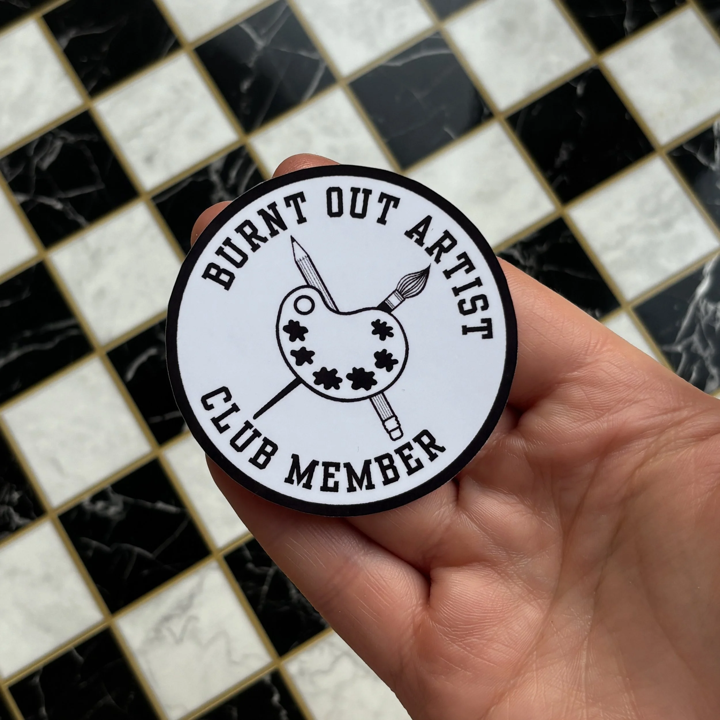 burnt out artist club member sticker holding over checkerboard.jpg