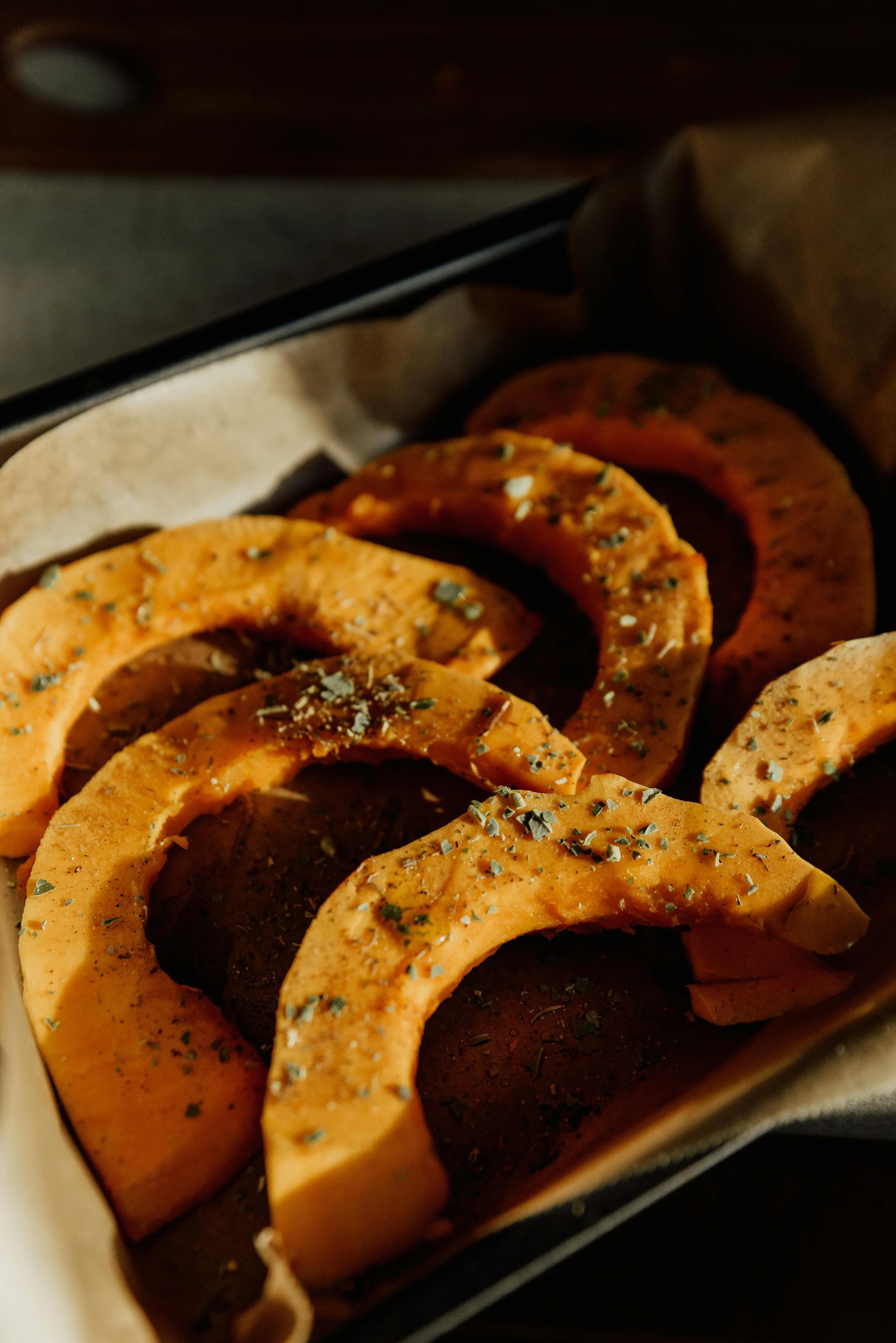 Seasoned squash slices arranged in a baking tray, ready for roasting.