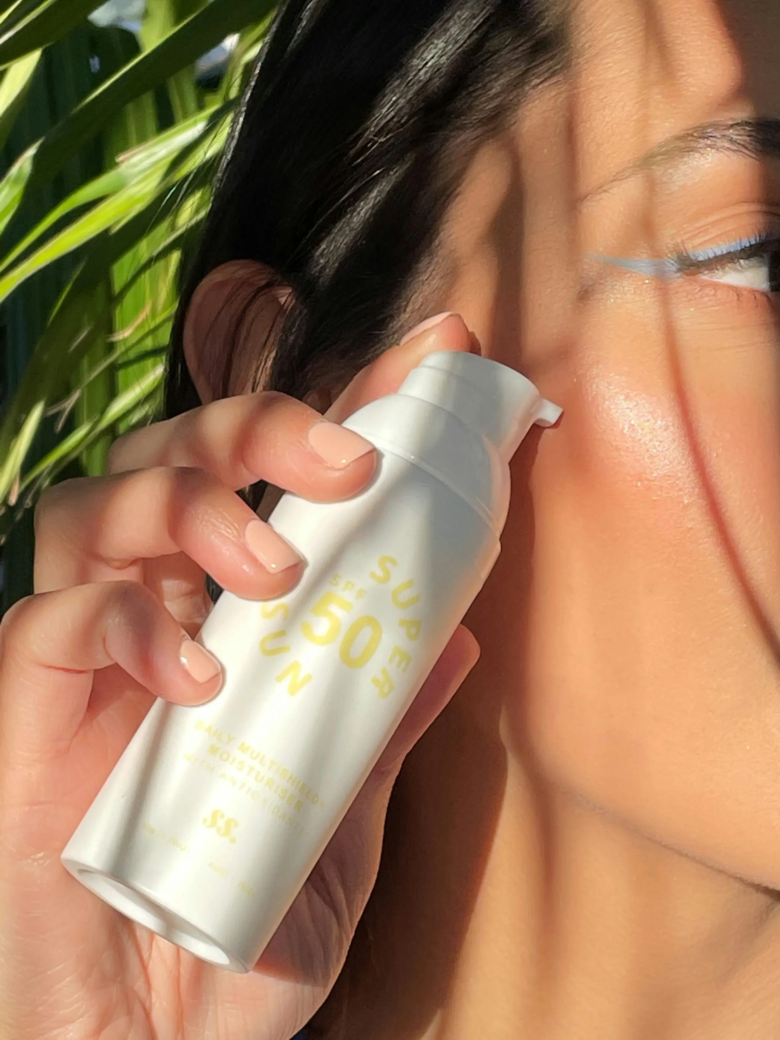 Model applies Sunny Skin Super Sun SPF 50 multitasking moisturizer pump in dappled sunlight.