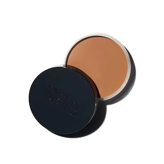  Saie Sun Melt cream bronzer compact opened to reveal warm brown shade; matte black lid rests ajar. 