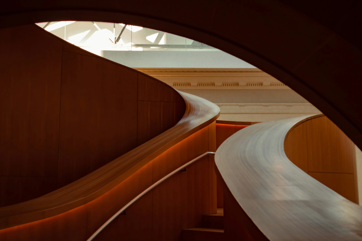 Curving, sculptural wooden staircase and ramp inside a modern museum, accented by warm indirect lighting (concept image, not Orient Express Corinthian).