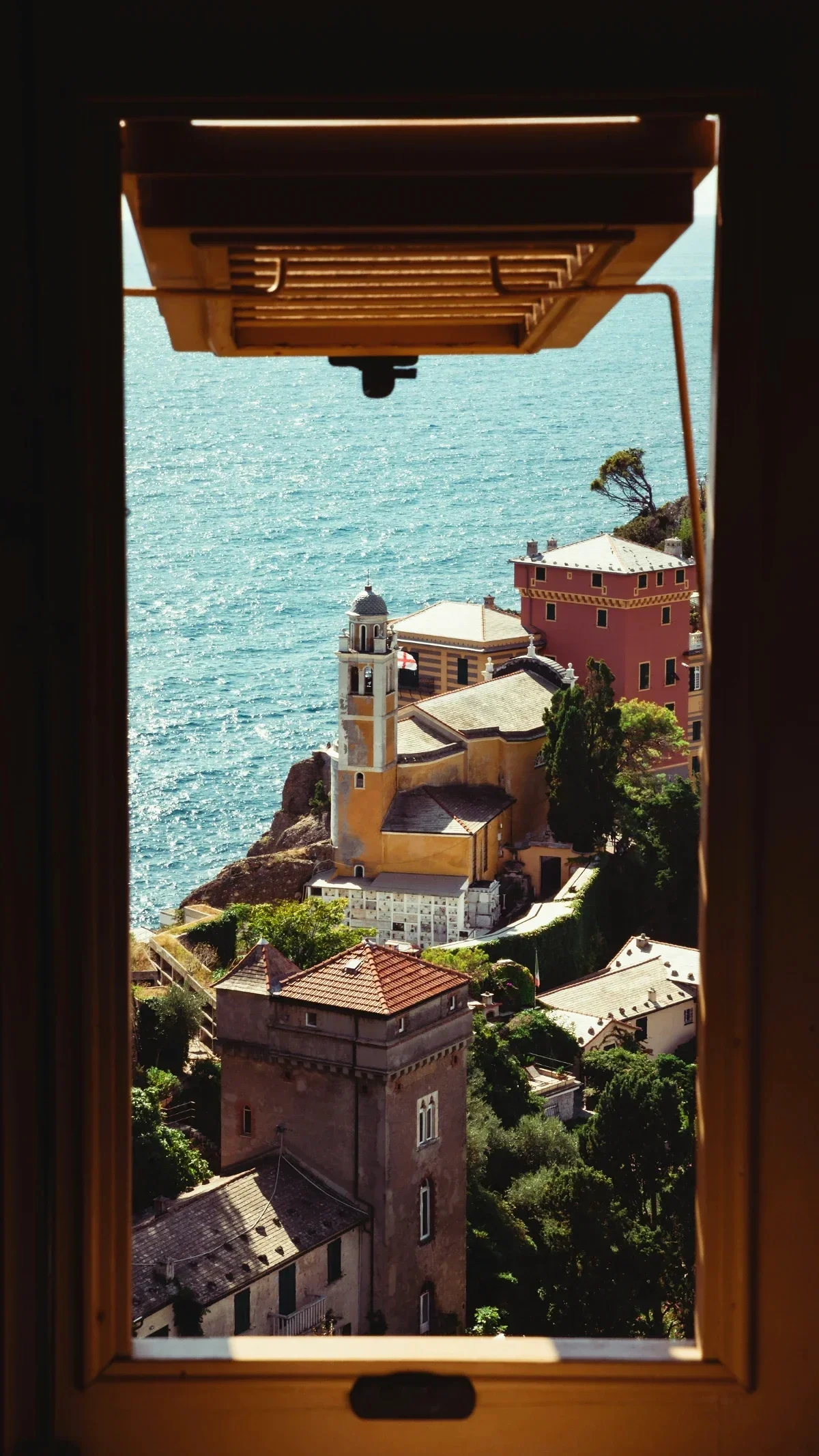 Seaside Ligurian village and turquoise water framed by an open window in golden afternoon light.