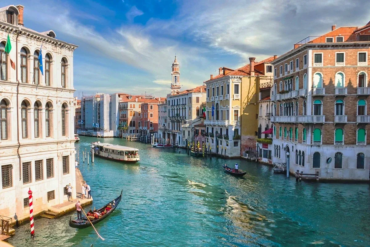  Gondola and vaporetto glide along the Grand Canal of Venice, framed by Renaissance palazzi and a bright blue sky. 