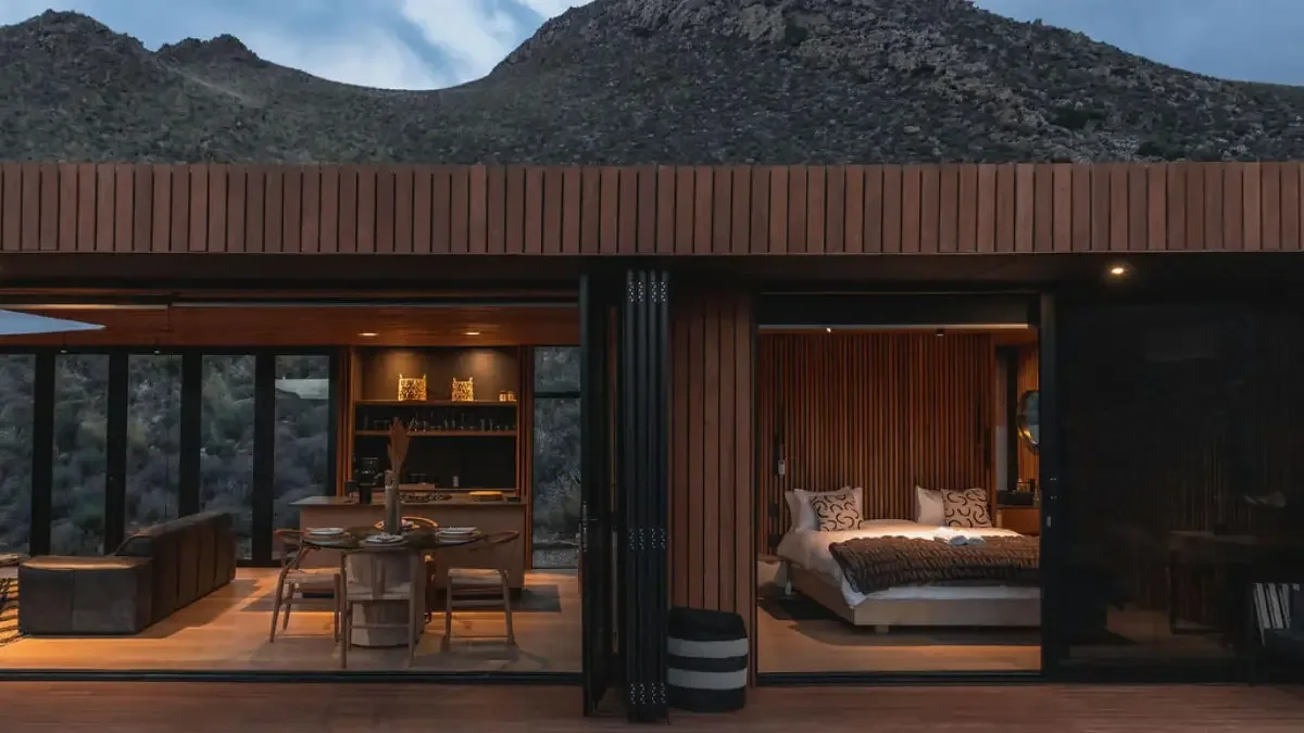 Cozy bedroom inside Yellowstone Cabin with dark shou sugi ban walls, fur throw and glass doors opening to deck, Breede River.