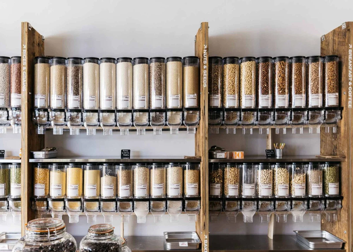 Wall of clear gravity bins filled with assorted grains, nuts and seeds in a tidy bulk grocery display.