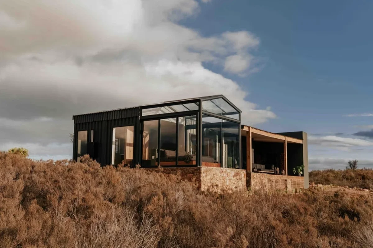 Copia Eco Cabins in the Overberg with glass-fronted design set on fynbos-covered hillside under open sky.