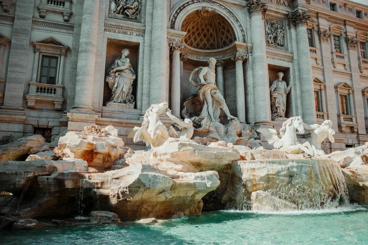  Baroque sculptures and turquoise pool of Trevi Fountain with water cascading over travertine rocks. 