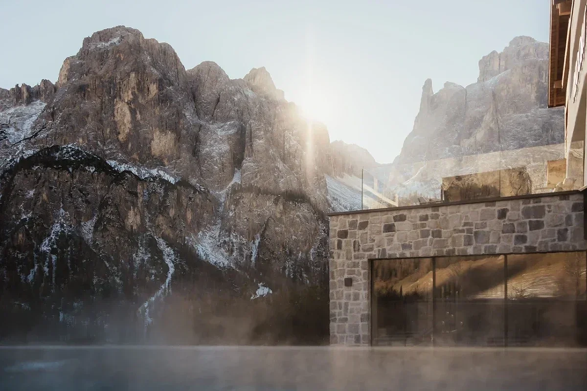  Hotel Recort in Alta Badia with outdoor pool and Dolomite peaks rising behind. 