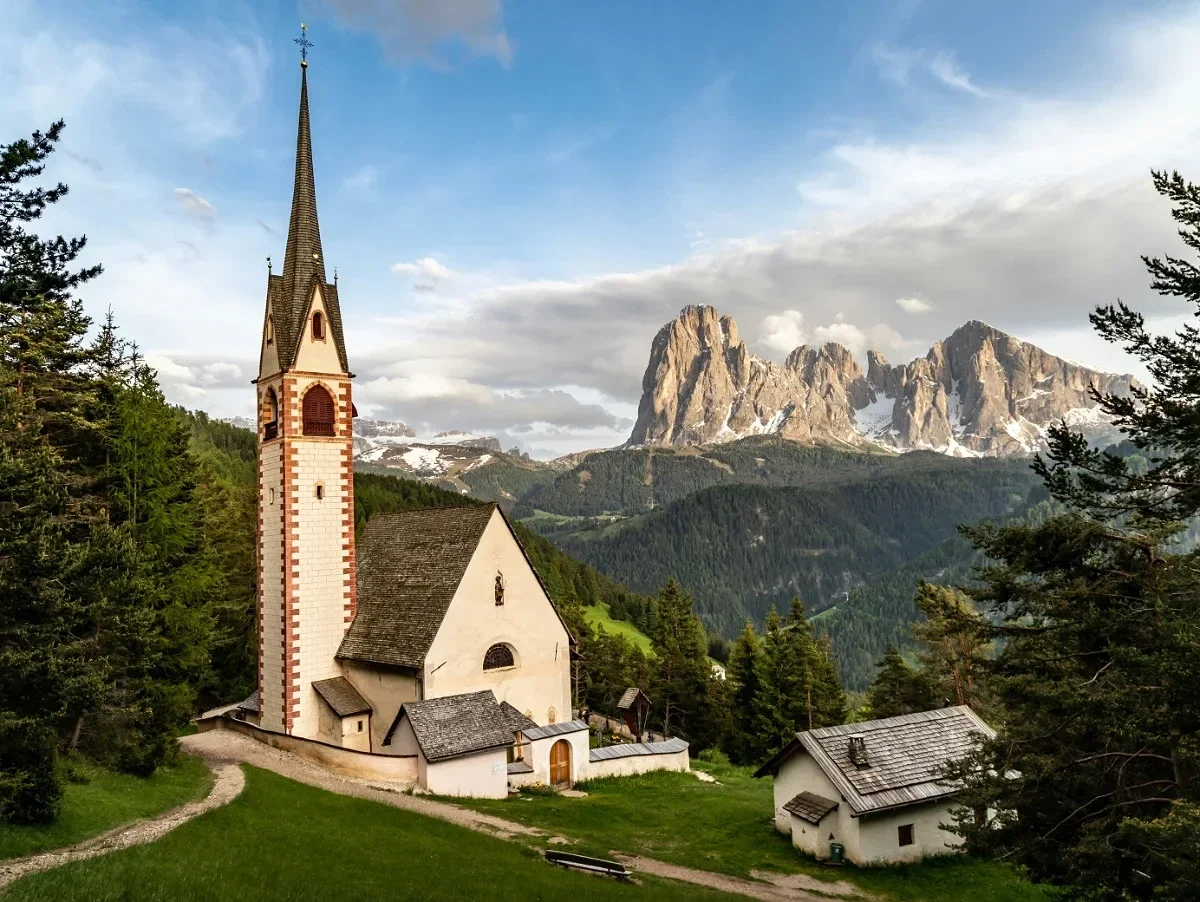  St John Church in Ranui with iconic Dolomite peaks rising behind alpine meadow. 