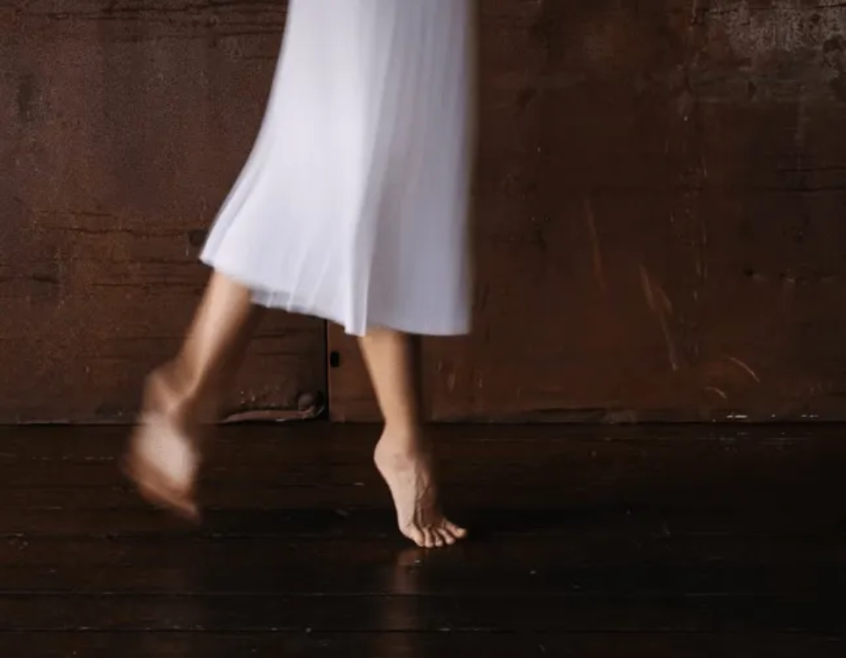 Blurred motion of a woman dancing across a dark wooden floor.