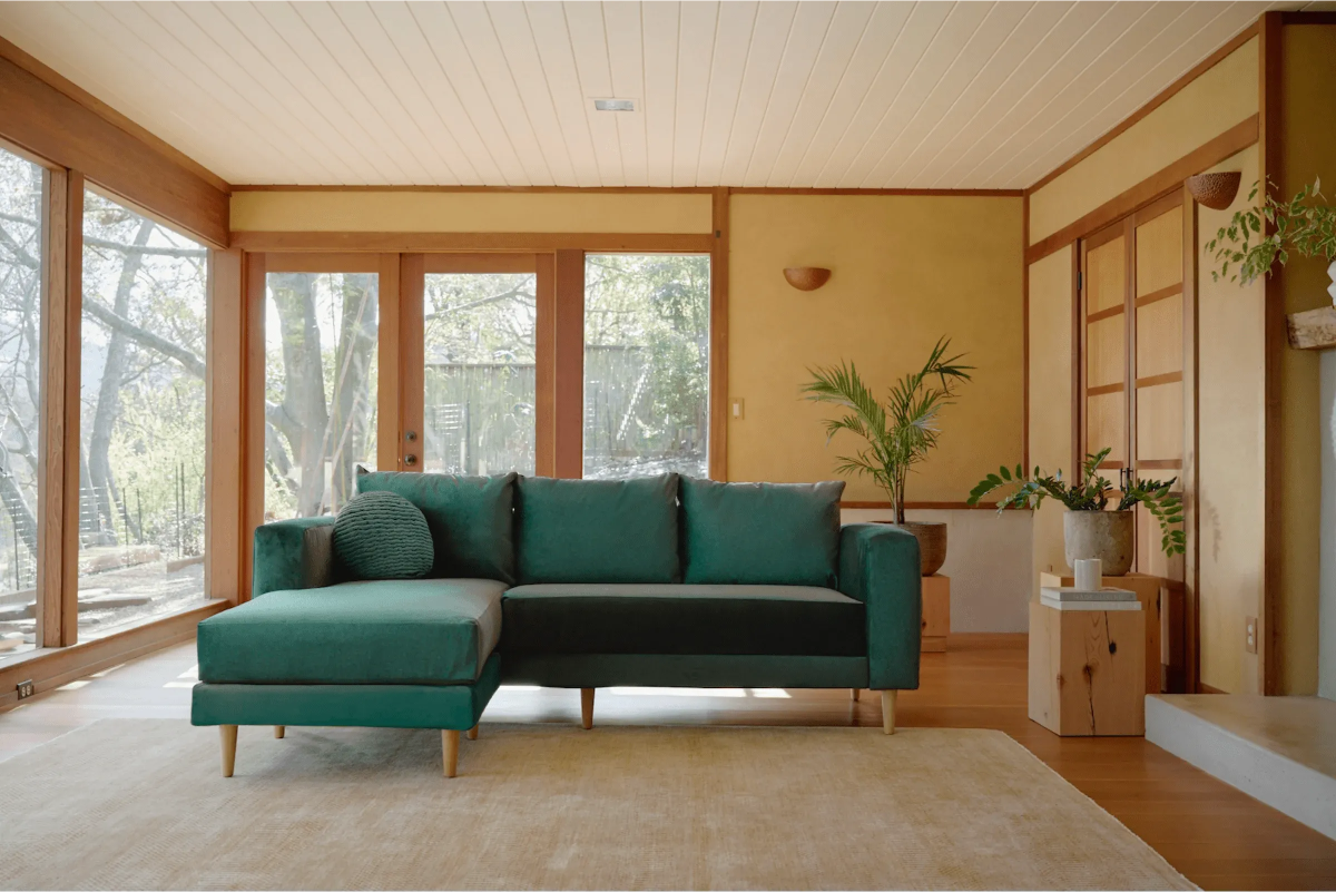 Deep green Sabai sectional sofa in a warm wood-accented living room.
