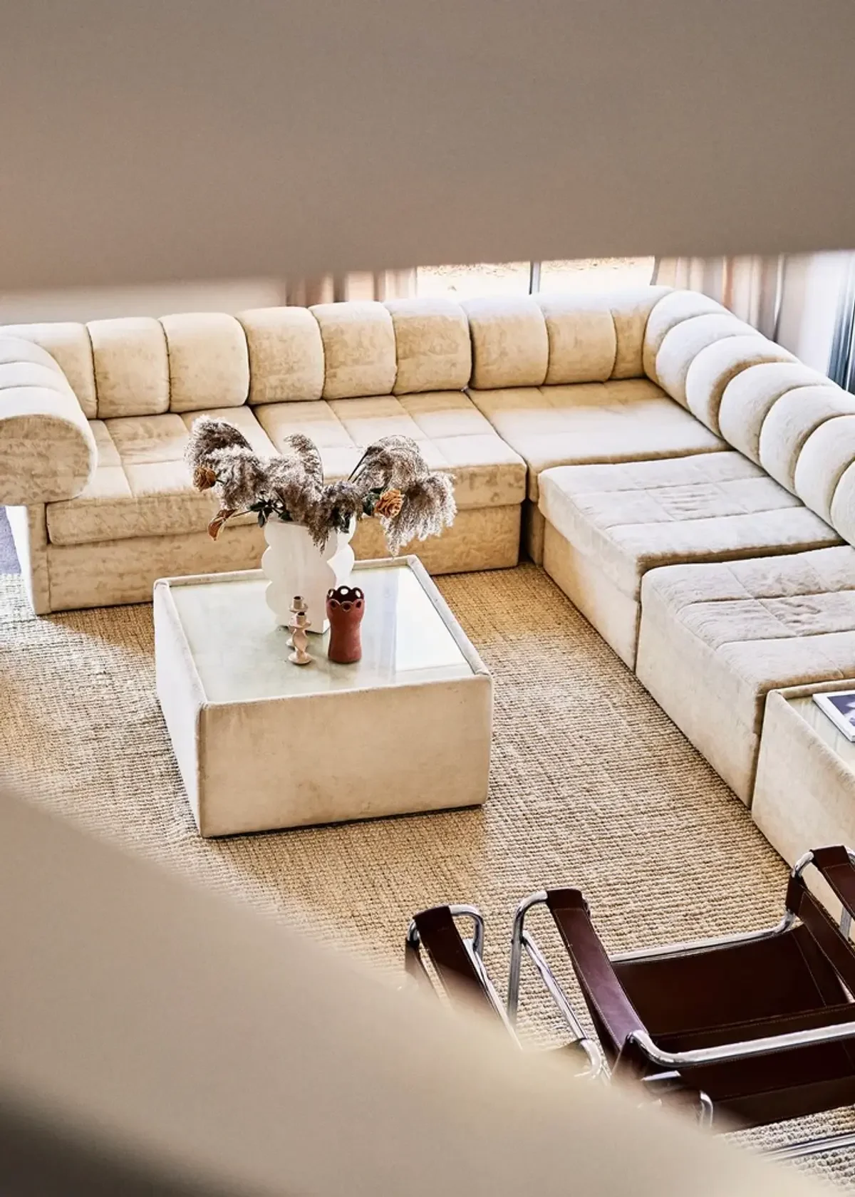 Warm neutral living room with plush curved modular sofa, jute rug and sculptural coffee table styled with dried floral vase.