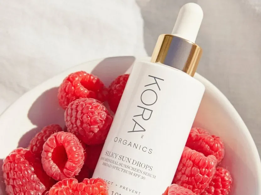 Kora Organics Silky Sun Drops mineral SPF 30 serum bottle nestled in fresh raspberries.