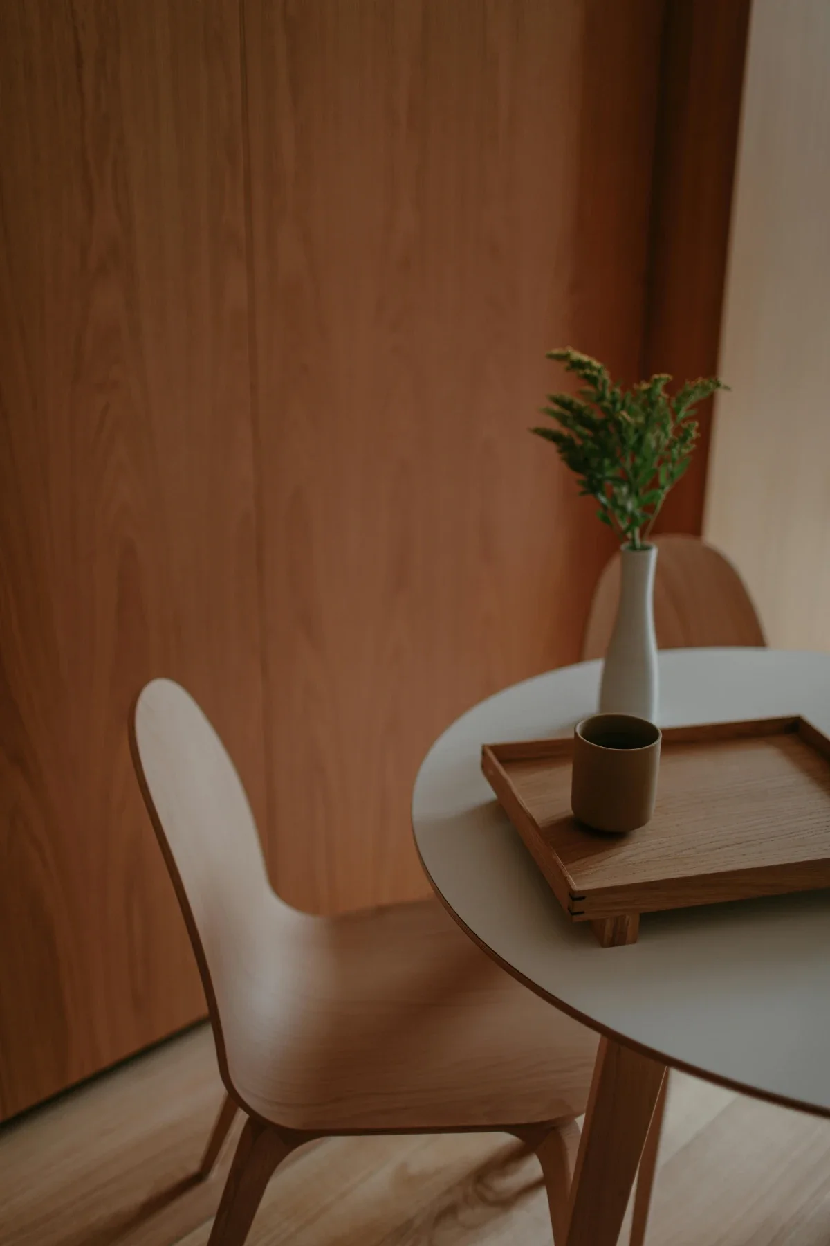 Scandinavian dining nook featuring a pale-oak chair beside a small round table with tray, mug and single-stem vase.