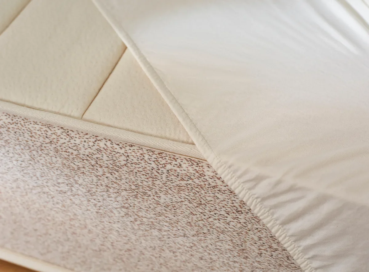  Close-up of Saatva waterproof organic mattress protector; corner flipped to show soft barrier lining. 