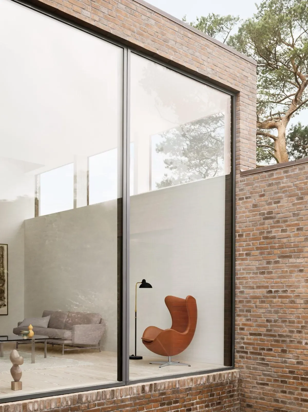 Light-filled modern brick house revealing brown Egg chair, neutral sofa and minimalist living room inside.