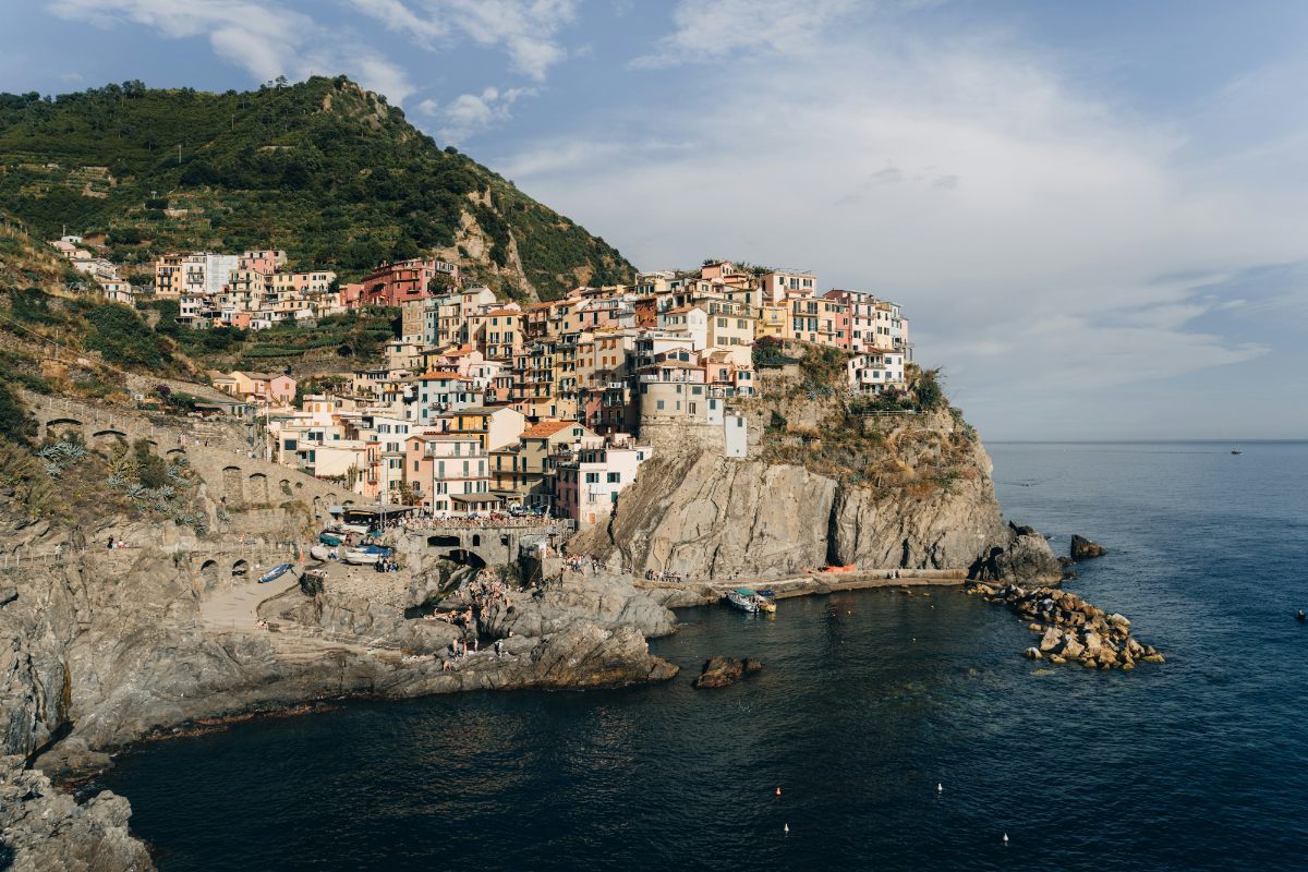 Colorful cliffside village houses stacked above deep blue sea under clear Ligurian sky.