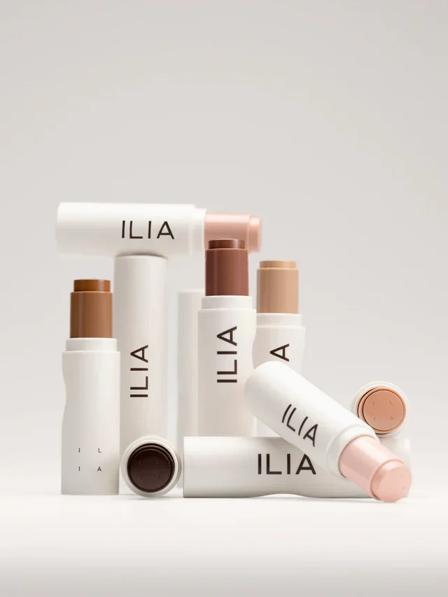  Assorted ILIA Skin Rewind Complexion Sticks in multiple shades, sleek white tubes stacked artfully on a neutral backdrop. 