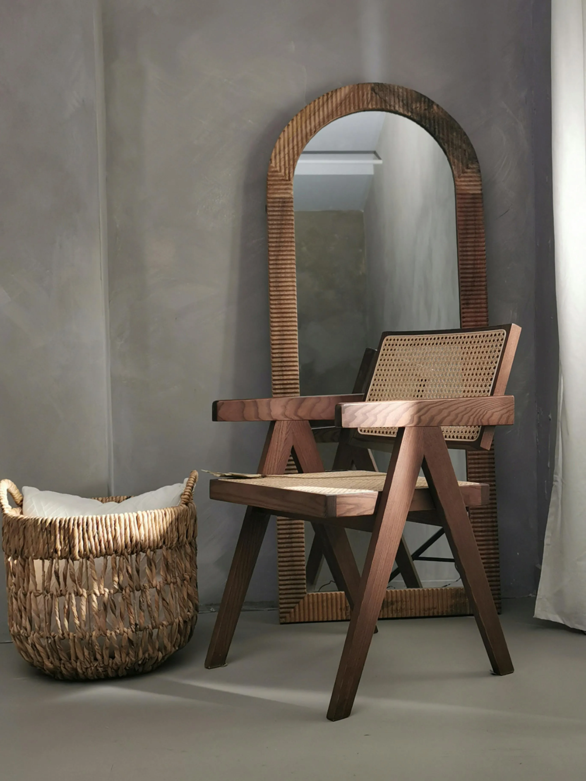 Mirror with woven frame and chair in minimalist space.