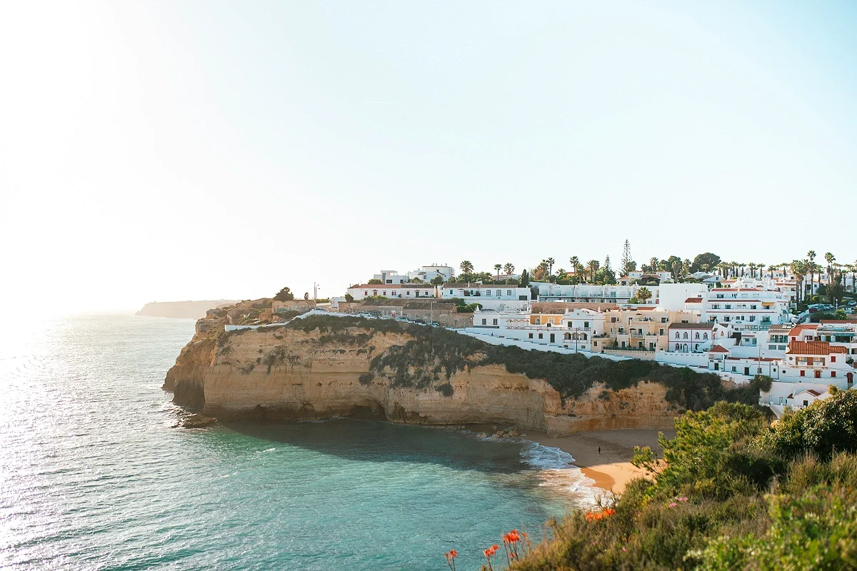 Sun-lit whitewashed clifftop village of Carvoeiro overlooking a small sandy cove and emerald Atlantic waters.