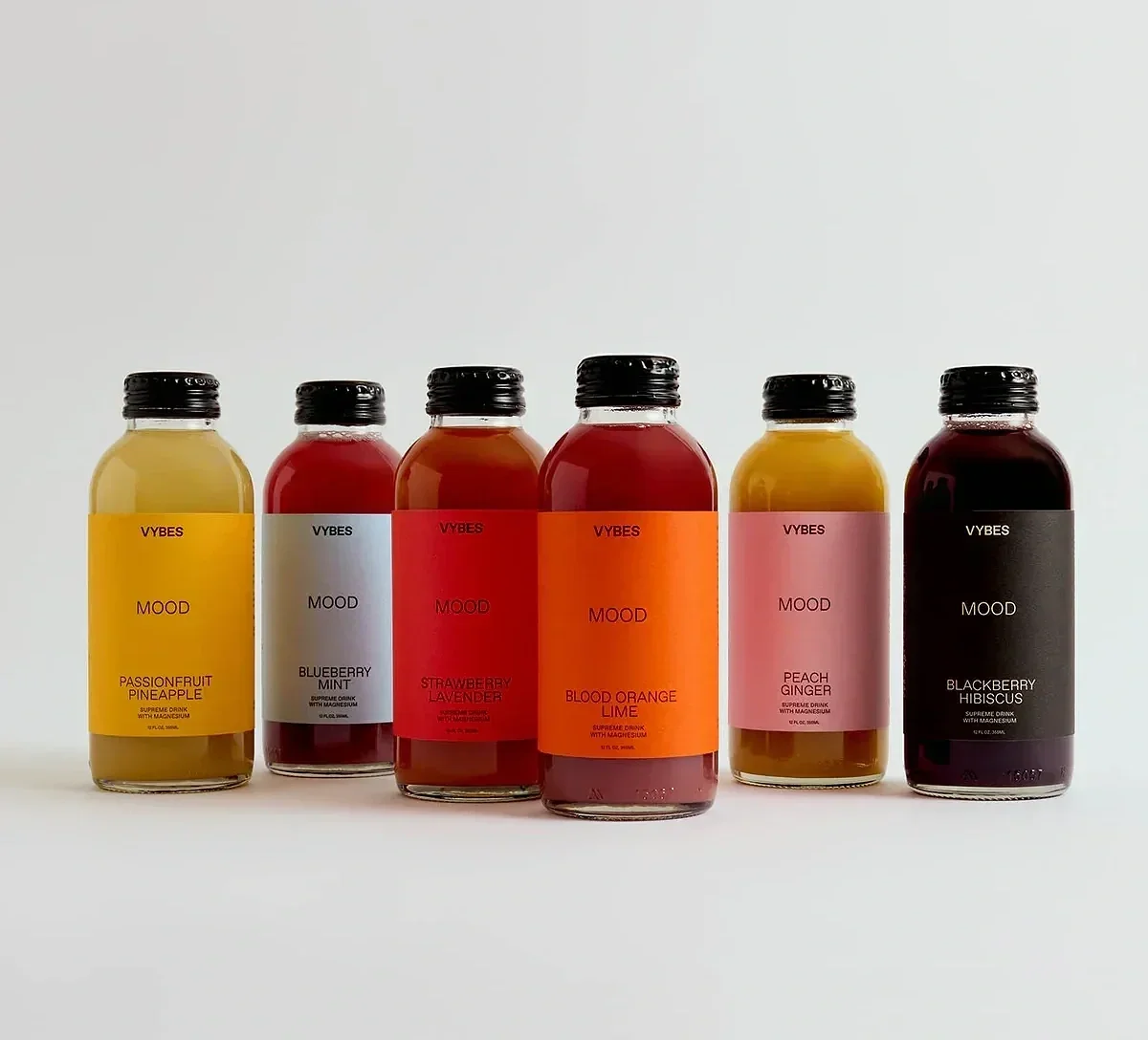  Six Vybes Mood functional beverage bottles with colorful labels and black caps arranged side by side on a neutral surface. 