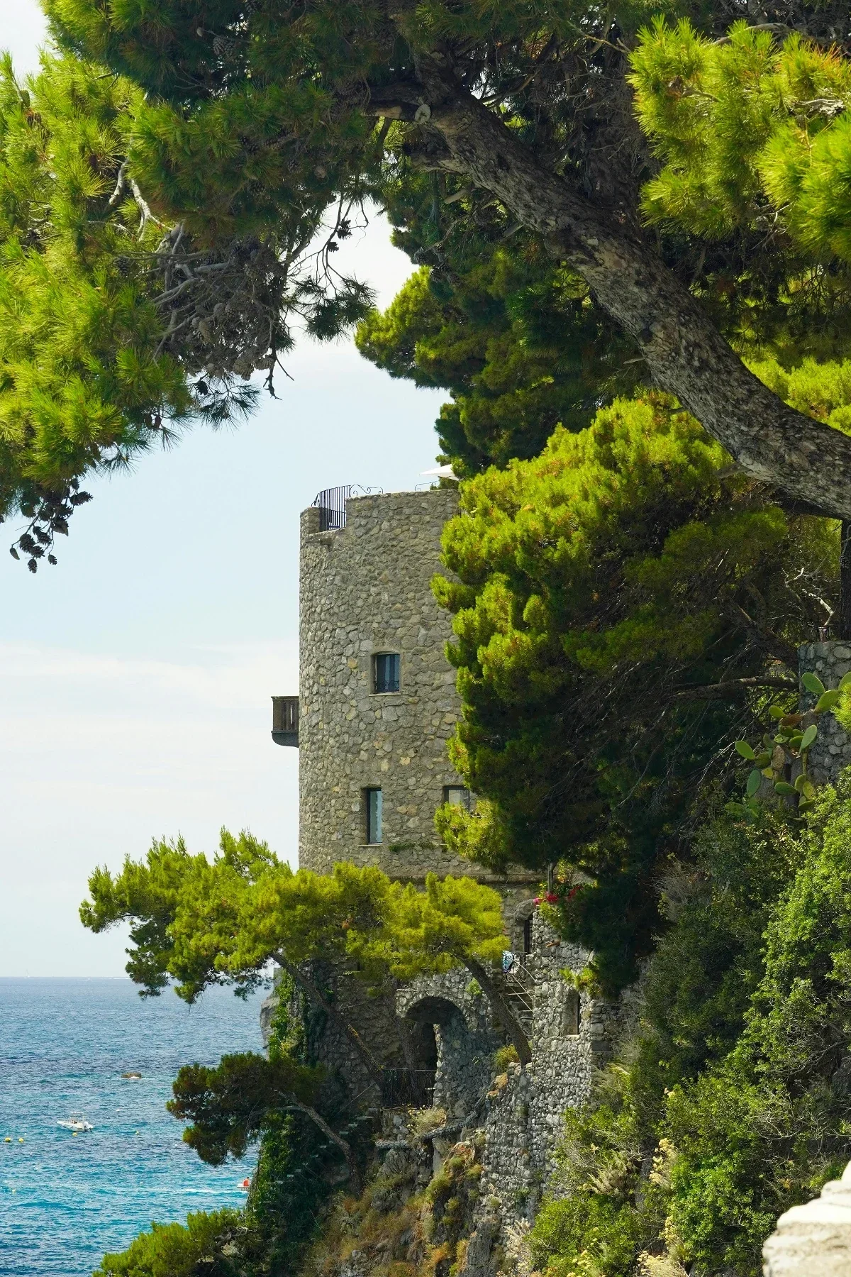 Medieval stone watchtower peeks through pine branches along dramatic Amalfi Coast cliffs near Positano.
