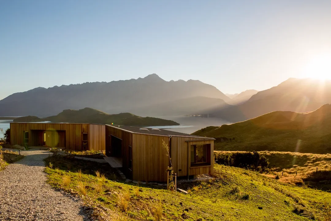 Timber eco-lodge at Aro Ha retreat overlooks Lake Wakatipu and the Southern Alps at golden sunrise.