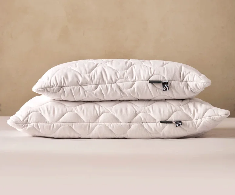 Pair of quilted washable wool pillows from Woolroom, light oatmeal tone against warm plaster wall.