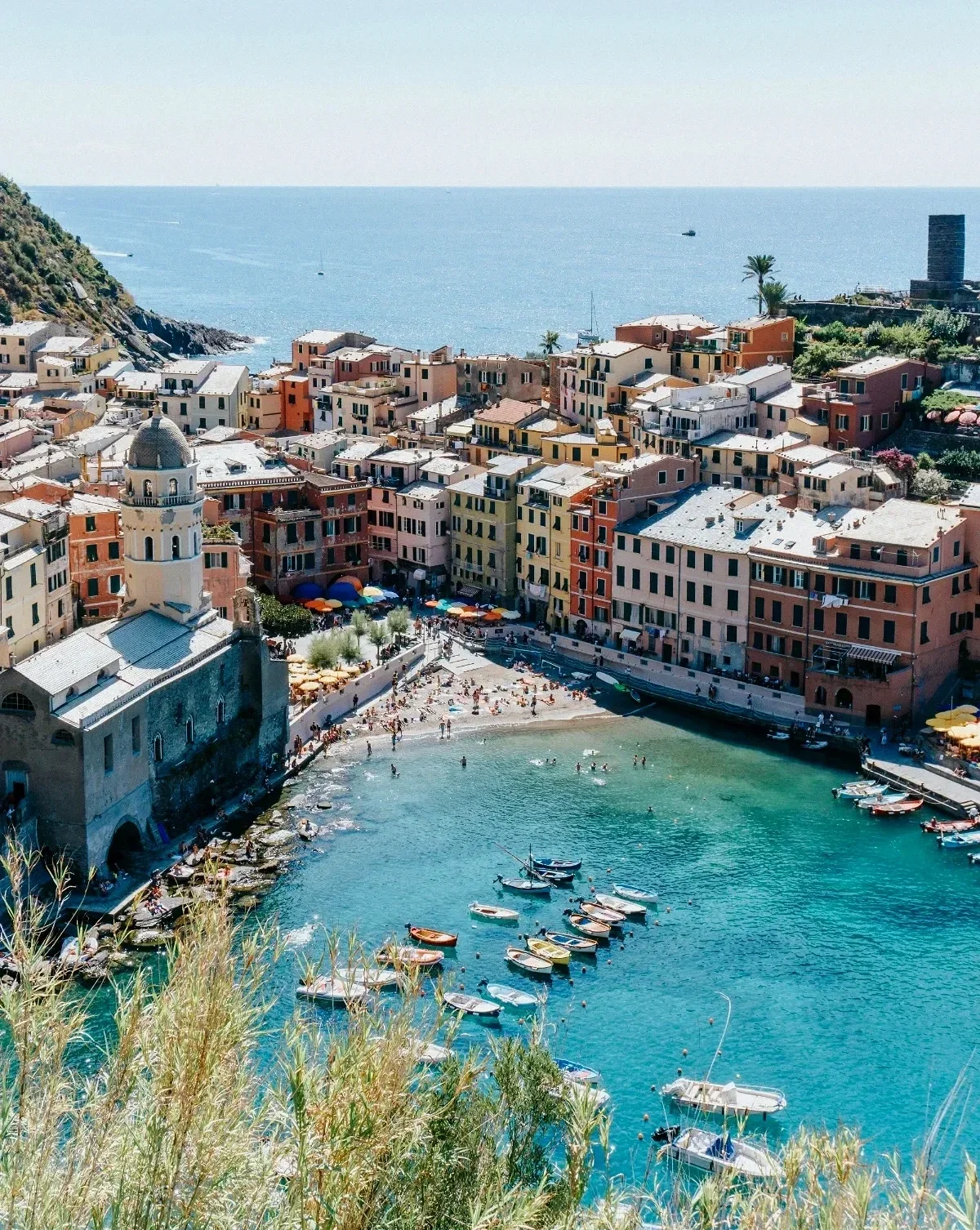  Sunlit Vernazza bay with swimmers, bobbing boats and pastel houses encircling the tiny beach on Cinque Terre coast. 