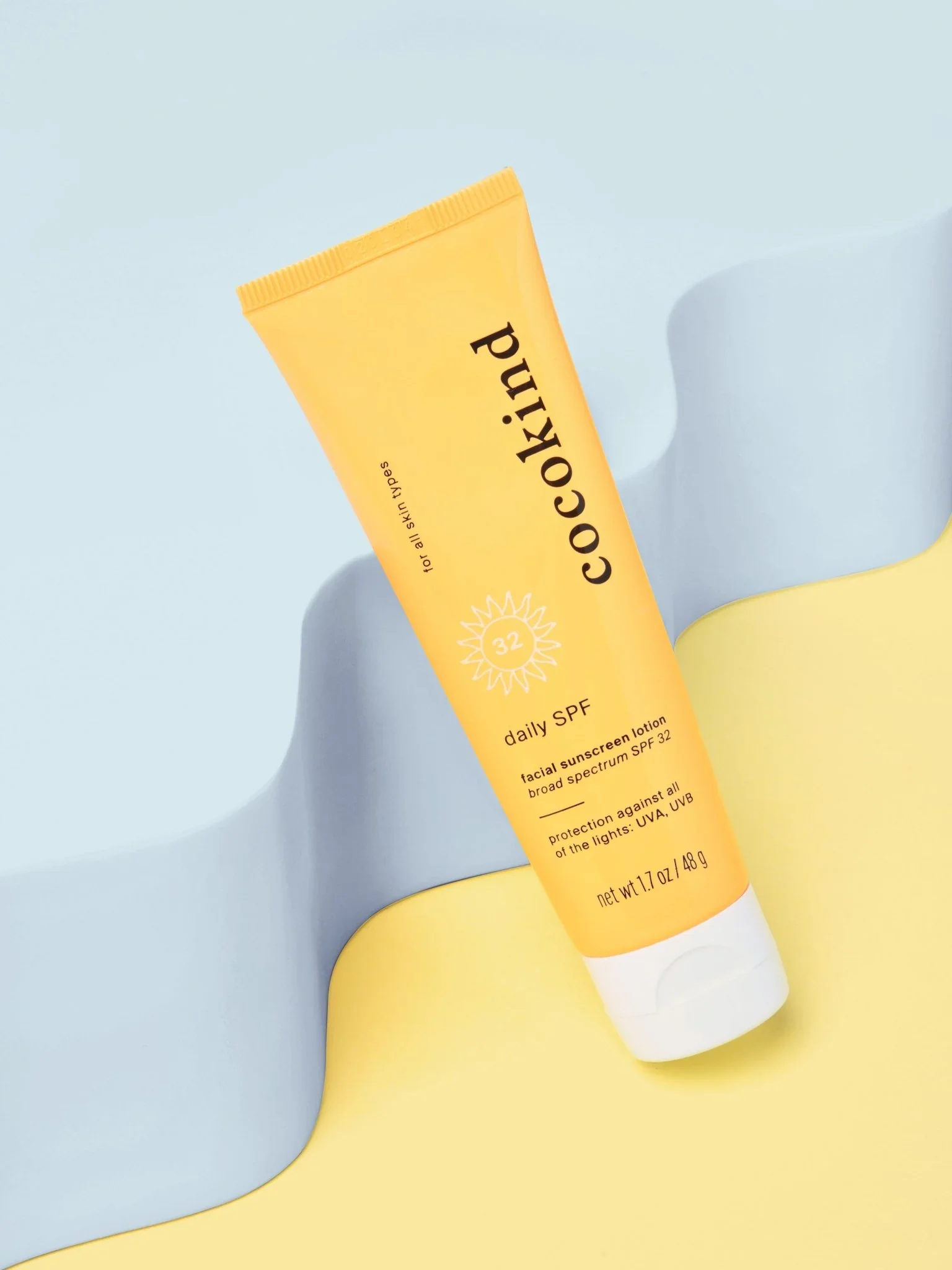 Bright yellow Daily SPF 32 tube by Cocokind styled on soft pastel backdrop.