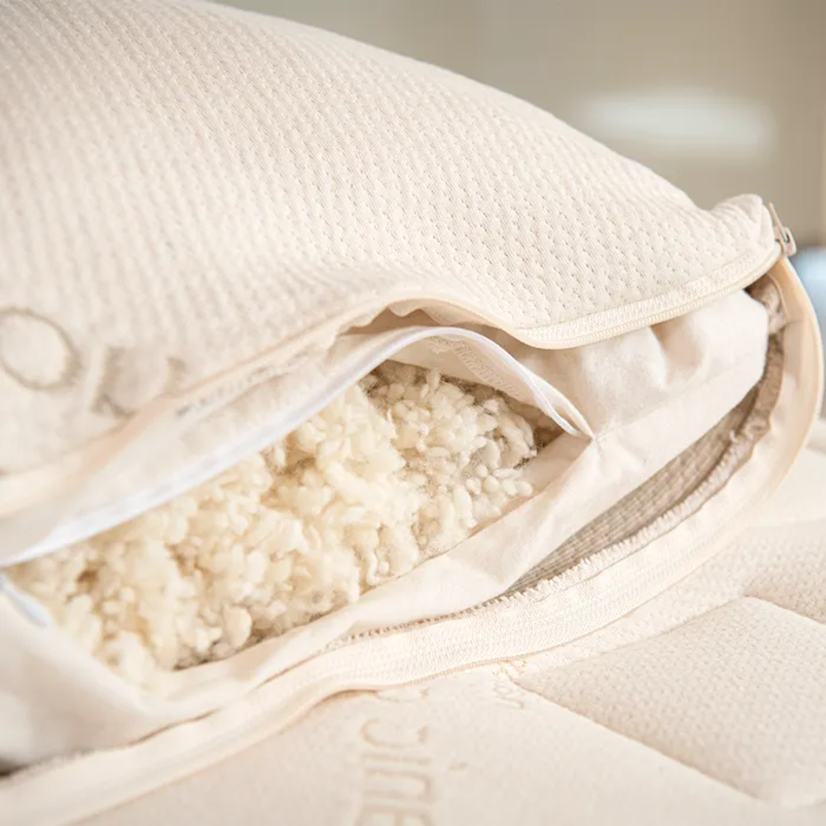 Zip-open Naturepedic pillow revealing adjustable organic wool fill inside textured cotton cover.