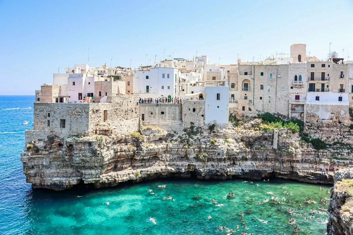  Cliff-top white stone houses of Polignano a Mare overlook swimmers in the clear turquoise Adriatic. 