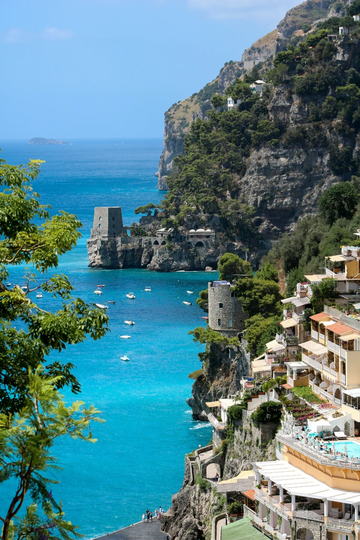 Turquoise Tyrrhenian Sea below dramatic Amalfi Coast cliffs dotted with towers, boats and pastel villas.