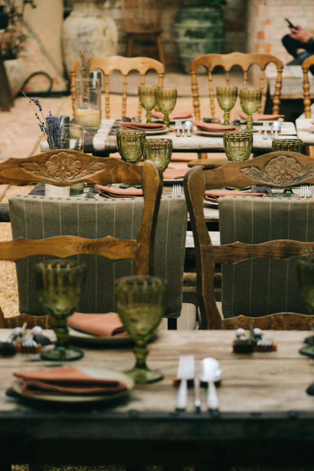 Long rustic table outdoors, vintage chairs, green goblets and linens await a farm-to-table meal.