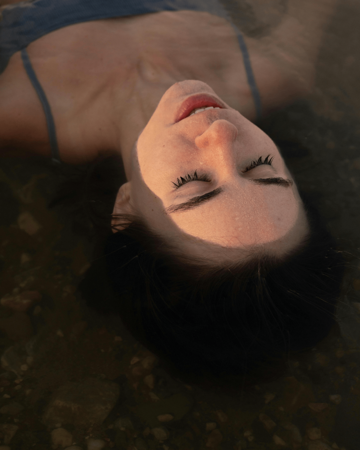 Woman floating on her back, eyes closed and face softly lit.