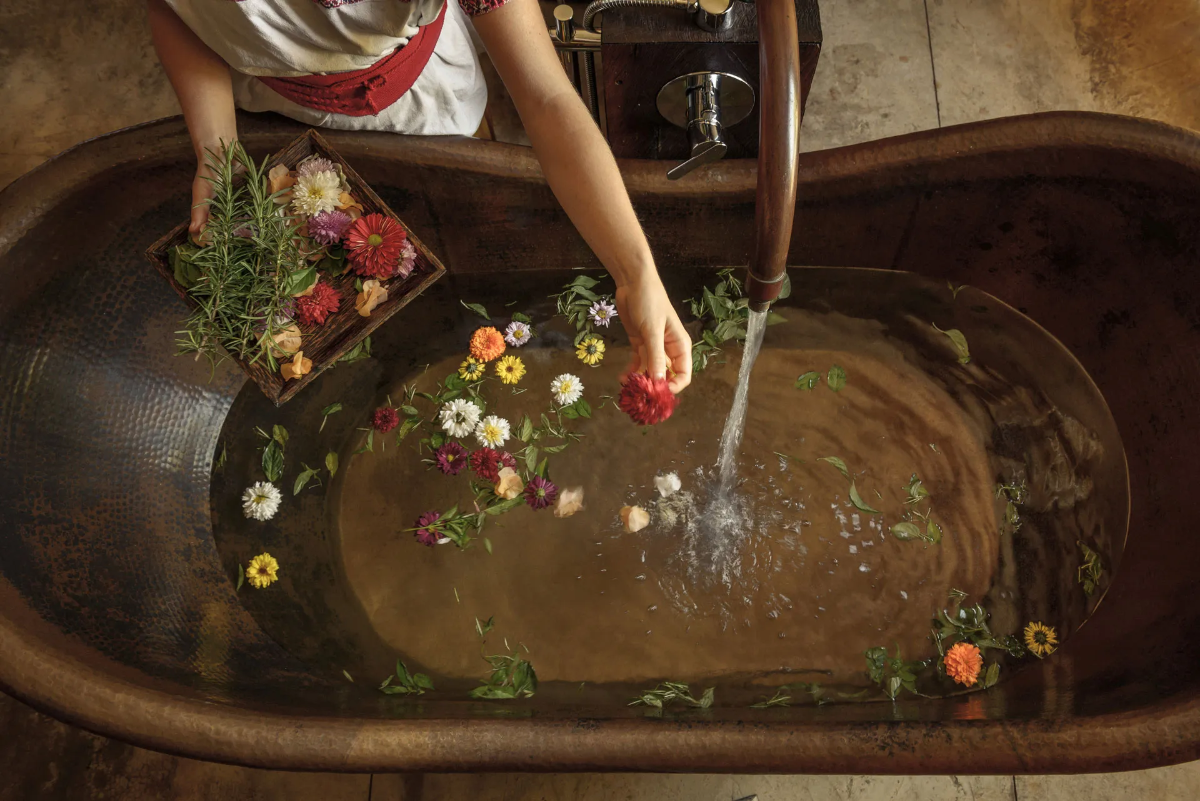  Therapist sprinkles colorful blossoms and herbs into a hand-hammered copper tub filling with warm spa water. 