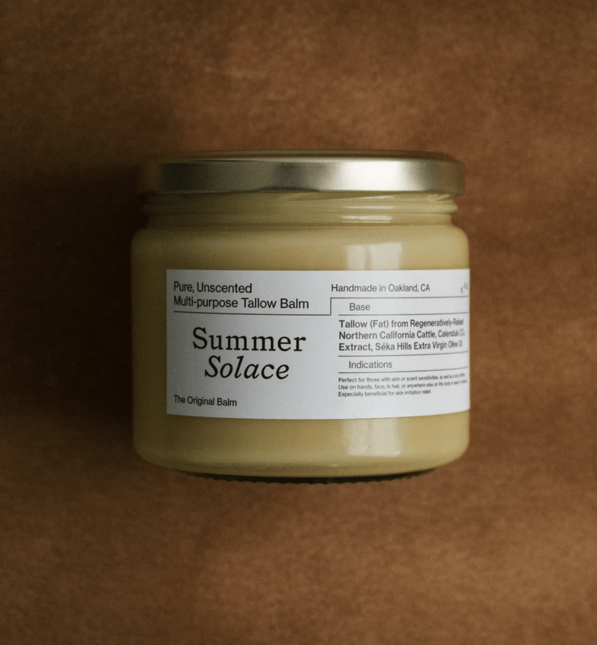 Summer Solace Original Balm, unscented multi-purpose tallow balm in a glass jar with gold lid against suede backdrop.