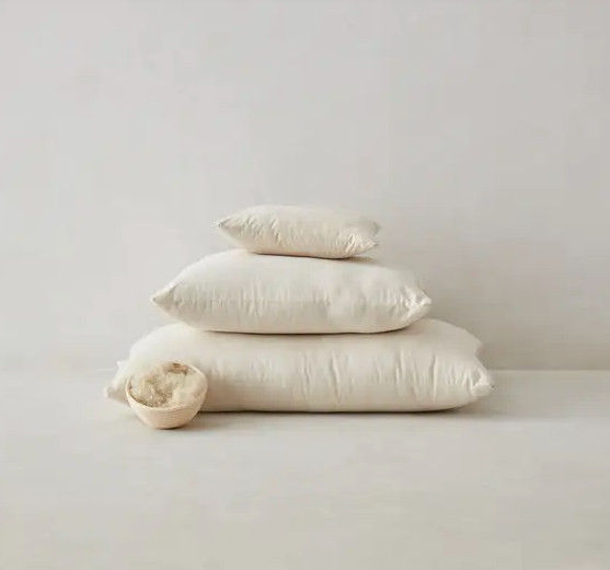 Group of neutral beige linen cushions, square, lumbar and bolster, arranged on minimalist cream floor.
